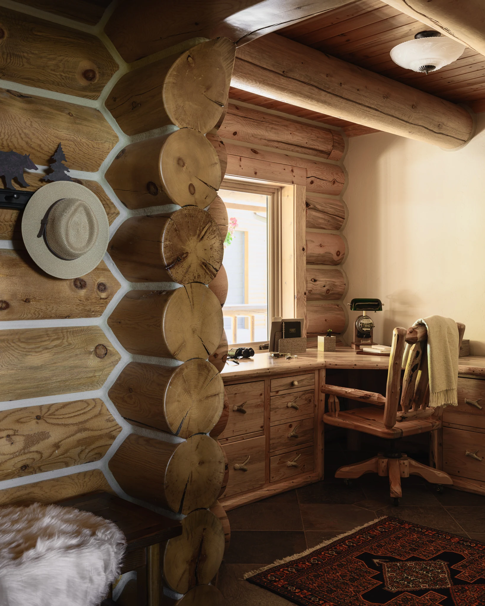Bedroom corner with a cowboy hat hanging on log walls beside a built-in desk — interior design photography Livingston Montana, Bear Canyon Ranch